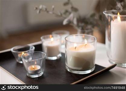 decoration, hygge and cosiness concept - burning white fragrance candles on tray on table at cozy home. burning fragrance candles on table at cozy home