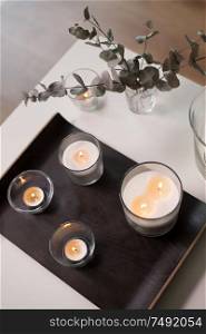 decoration, hygge and cosiness concept - burning white fragrance candles on tray and branches of eucalyptus populus on table. candles and branches of eucalyptus on table