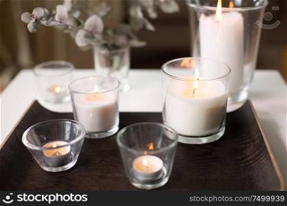 decoration, hygge and cosiness concept - burning white fragrance candles on tray and branches of eucalyptus populus on table at cozy home. burning fragrance candles on table at cozy home