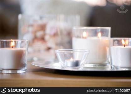 decoration, hygge and cosiness concept - burning white fragrance candles on tray on table. burning white fragrance candles on tray on table
