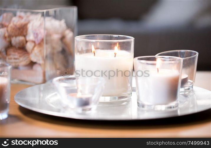 decoration, hygge and cosiness concept - burning white fragrance candles on tray on table. burning white fragrance candles on tray on table