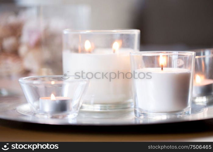 decoration, hygge and cosiness concept - burning white fragrance candles on tray on table. burning white fragrance candles on tray on table