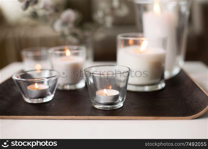 decoration, hygge and cosiness concept - burning white fragrance candles on tray table at cozy home. burning fragrance candles on table at cozy home