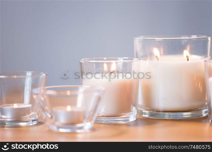decoration, hygge and cosiness concept - burning white fragrance candles on wooden table. burning white fragrance candles on wooden table