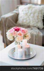 decoration, hygge and cosiness concept - candles burning on table and flowers at cozy home. candles burning on table and flowers at cozy home