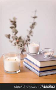 decoration, hygge and cosiness concept - fragrance candles burning in glass holders and books on wooden table. fragrance candles burning and books on table
