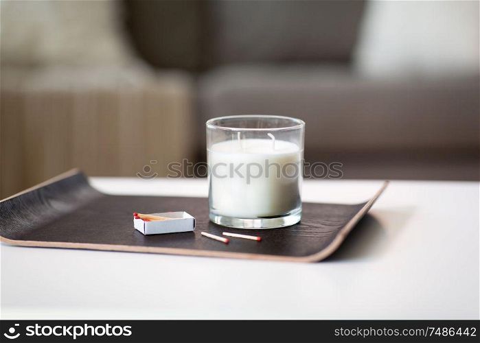 decoration, hygge and cosiness concept - white fragrance candle and matches on tray on table at home. fragrance candle and matches on tray on table