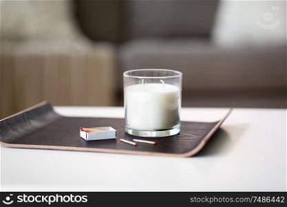 decoration, hygge and cosiness concept - white fragrance candle and matches on tray on table at home. fragrance candle and matches on tray on table