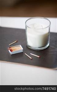 decoration, hygge and cosiness concept - white fragrance candle and matches on tray on table. fragrance candle and matches on tray on table