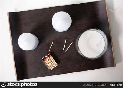 decoration, hygge and cosiness concept - white fragrance candlesand matches on tray on table. fragrance candles and matches on tray on table