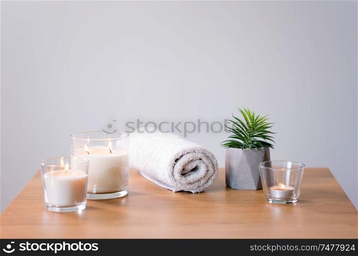 decoration, hygge and spa concept - burning white fragrance candles, bath towel and succulent on table. burning fragrance candles and bath towel on table
