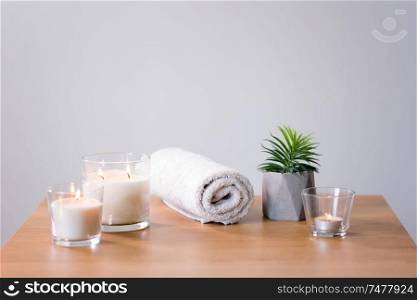 decoration, hygge and spa concept - burning white fragrance candles, bath towel and succulent on table. burning fragrance candles and bath towel on table