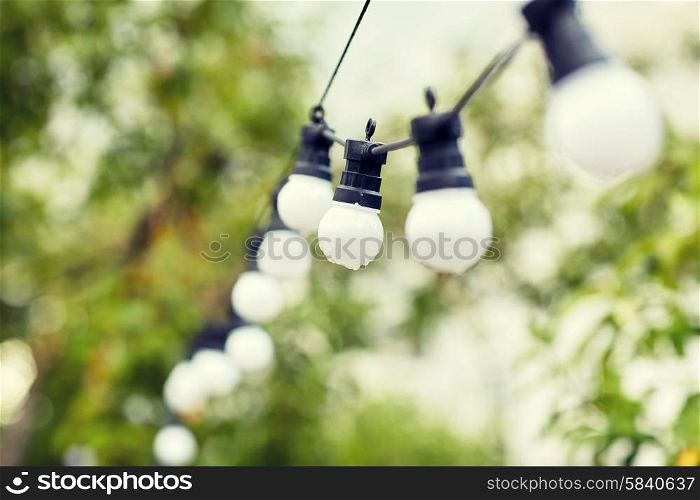 decoration, illumination, electricity, holidays and lightning concept - close up of electric bulb garland hanging in rainy summer garden