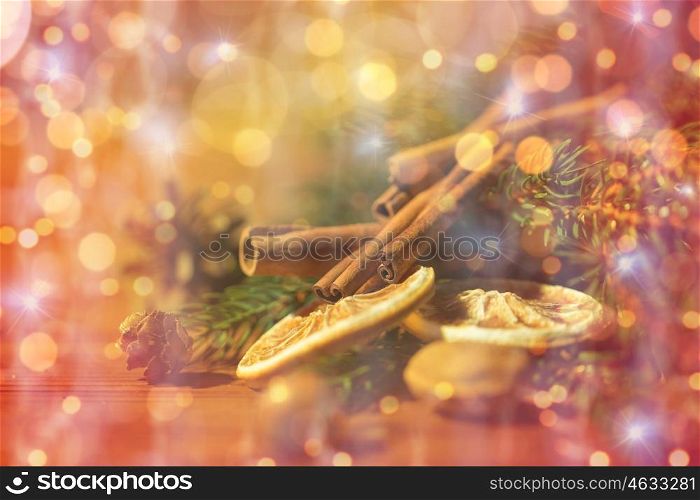 decoration, winter, holidays and new year concept - close up of christmas fir branch with cinnamon and dried orange on wooden table over lights