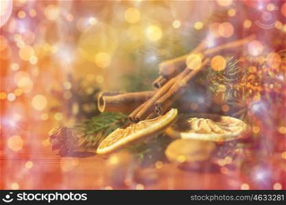 decoration, winter, holidays and new year concept - close up of christmas fir branch with cinnamon and dried orange on wooden table over lights