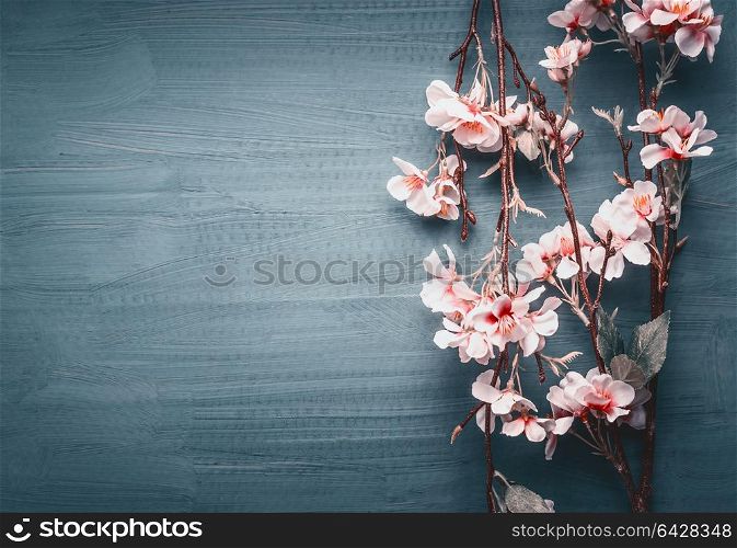Decorative artificial spring blossom on dark blue background, top view, border
