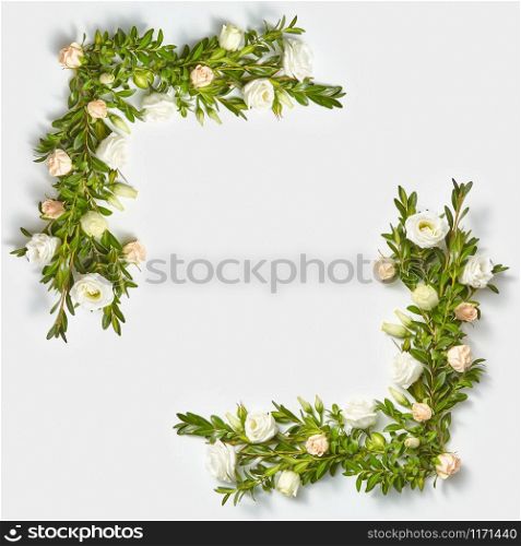 Decorative blossoming corner frame from evegreen leaves banches and little flowers on a light grey background with copy space. Flat lay. Valentine&rsquo;s Day concept.. Square corner frame from boxwood twigs and flowers.