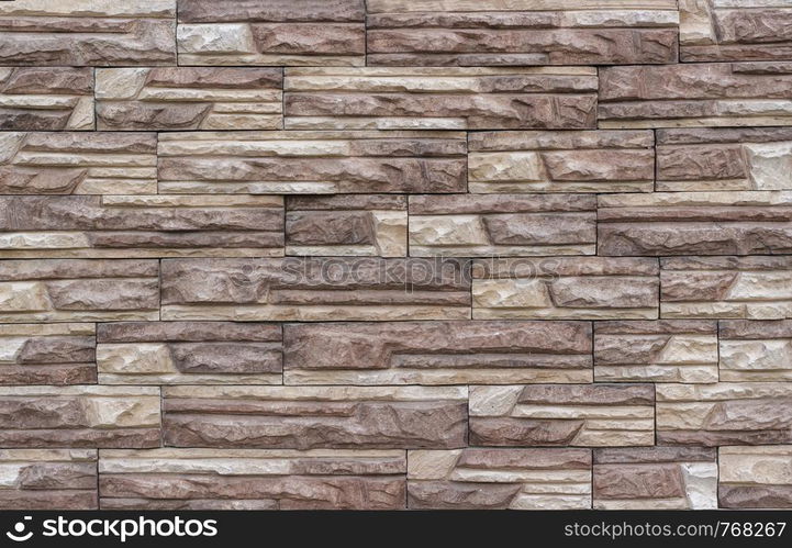 Decorative brick wall as background or texture. Artificial facing torn stone in beige and brown tones in a geometric pattern.