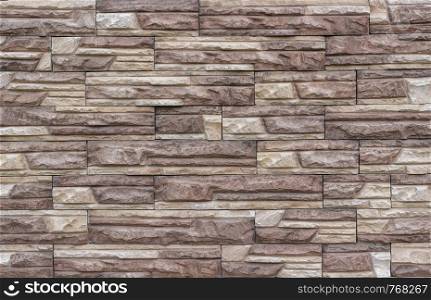 Decorative brick wall as background or texture. Artificial facing torn stone in beige and brown tones in a geometric pattern.