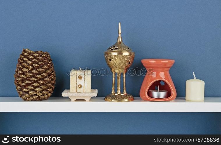 Decorative candles on white shelf on blue wallpaper background