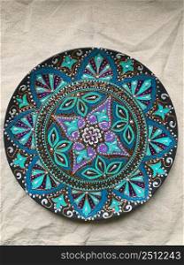 Decorative ceramic plate with  different colors. painted plate on white background, closeup, top view. Decorative porcelain plate painted with acrylic paints, handwork, dot painting