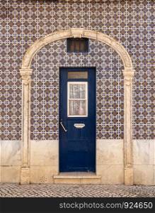 Decorative ceramic tiles on around a blue door entrance to home in Alfama district of Lisbon, Portugal. Traditional ceramic tiles decorate exterior of large house in Lisbon