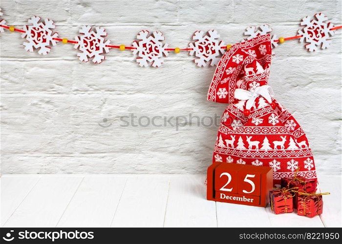 Decorative Christmas gift boxes and red gift bag with Christmas pattern with red wooden perpetual calendar with date 25 december on white brick wall background. Banner, header, mockup with copy space