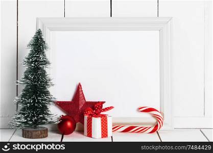Decorative Christmas tree candy cane , star , baubles and gift box and blank paper fith frame on white wooden background. Christmas decorations and frame