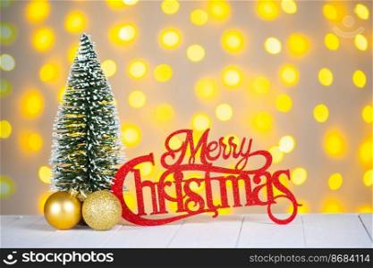 Decorative Christmas tree, golden balls and red wooden lettering Merry Christmas on defocused light bokeh background.. Christmas tree, golden balls and red wooden lettering Merry Christmas on light bokeh background.