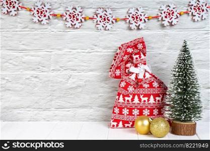 Decorative Christmas tree, red gift bag and golden balls on white wooden background with garland. Top view, flat lay with copy space, banner, header, New Year background. Decorative christmas tree, red gift bag and golden balls on white wooden background.
