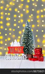 Decorative Christmas tree, red gift boxes and wooden lettering Merry Christmas on defocused light bokeh background. 