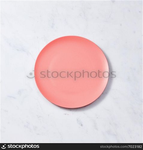 Decorative clay dish, covered with glazed in a color of the year 2019 Living Coral pantone on a gray background. Traditional ceramic handcrafted. Can be used for display or montage your products.. Porcelain handmade empty plate in a color of the year 2019 Living Coral pantone on a gray marble table, place for text. Flat lay