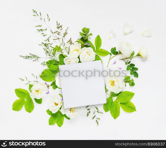 Decorative composition in retro style consisting of blank white paper card and white wild rose flowers with green leaves on white background. Top view, flat lay