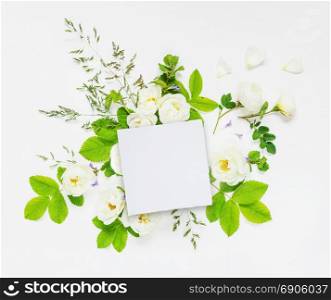 Decorative composition in retro style consisting of blank white paper card and white wild rose flowers with green leaves on white background. Top view, flat lay