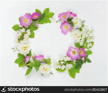 Decorative composition in retro style consisting of pink wild rose and white locust flowers with green leaves on white background. Top view, flat lay