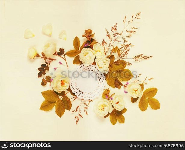 Decorative composition in retro style consisting of round white paper openwork doily and white wild rose flowers with green leaves on white background. Top view, flat lay. Mocap. Toned image
