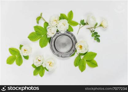 Decorative composition in retro style consisting of vintage metal tray ore retro plate and white rose flowers with green leaves on white background. Top view, flat lay
