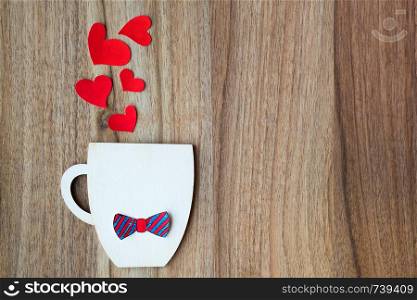 Decorative Cup with bow-tie and hearts on wooden background. Greeting card. Fathers day concept. Decorative Cup with paper bow-tie and red hearts on wooden background. Copyspace.