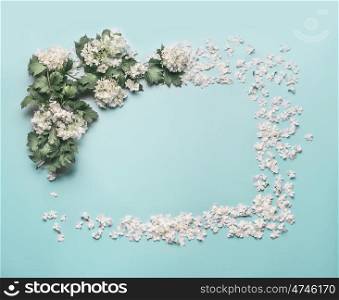Decorative floral frame made of white flowers, petals and blossom on pastel blue background. Spring and summer concept. Flat lay, top view. Invitation or card for wedding, birthday and other holidays
