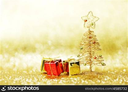 Decorative golden toy christmas tree and gifts on golden background