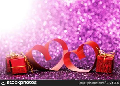 Decorative hearts of red ribbon and gifts on shiny glitter background
