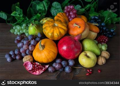 Decorative pumpkins, squash, apples, pears, pomegranates and grapes on the dark wooden background