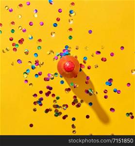 Decorative red painted bottle of wine with hard shadows and colorful confetti on an yellow background, copy space. Top view. Holiday greeting card. Top view of red painted bottle with confetti on yellow.
