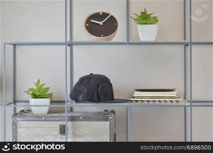 Decorative shelf on wall with books, black caps, wooden clock and vase