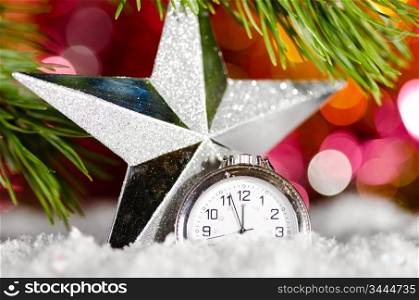 decorative star and clock on snow with christmas tree branch on blurred background