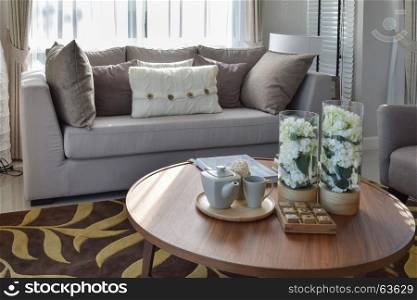 decorative tea set and glass vase on wooden round table in living room interior