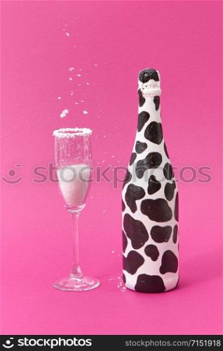 Decorative white painted wine bottle with black spots and glass with falling white powder on a hot pink background, place for text. Congratulation card.. White powder falls in a glass and painted black spots wine bottle.