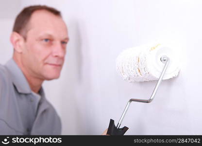 Decorator painting a room white with the roller in the foreground