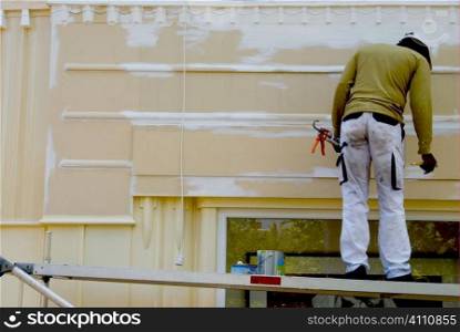 Decorator stands on plank painting building exterior, Holland