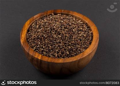 Decorticated cardamom seeds in a wooden bowl on dark stone background